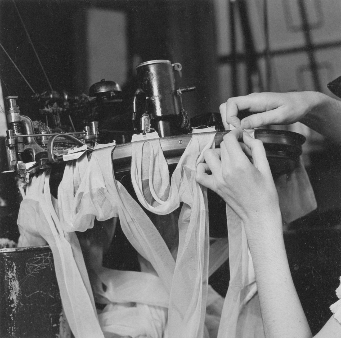 Mani di un operaio di fabbrica che aggiustano il tessuto su una macchina tessile industriale.