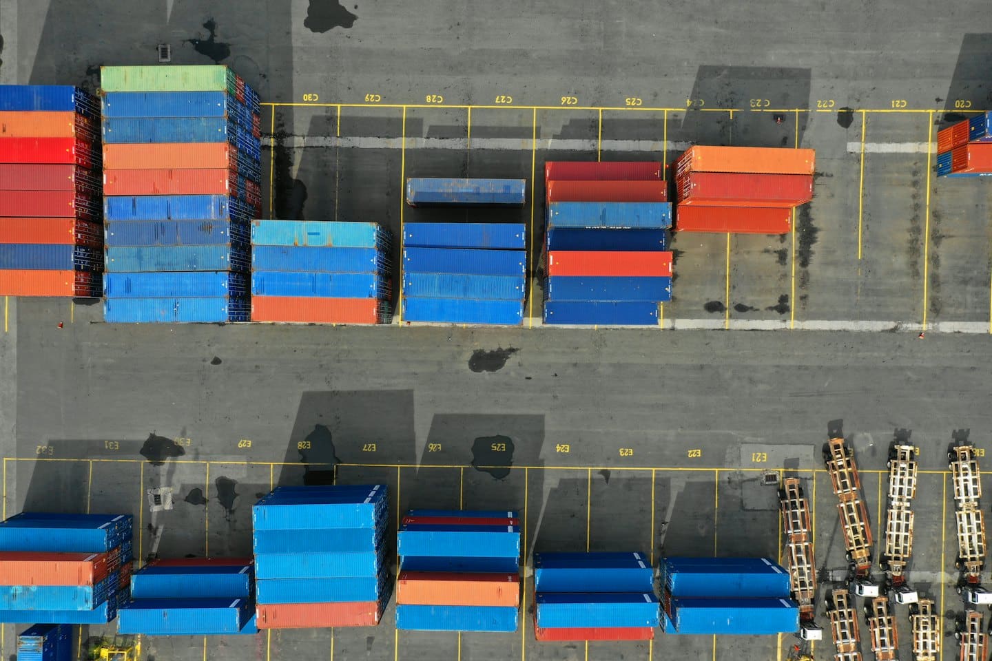 Vista aerea di un trafficato hub logistico con container marittimi blu e rossi impilati.